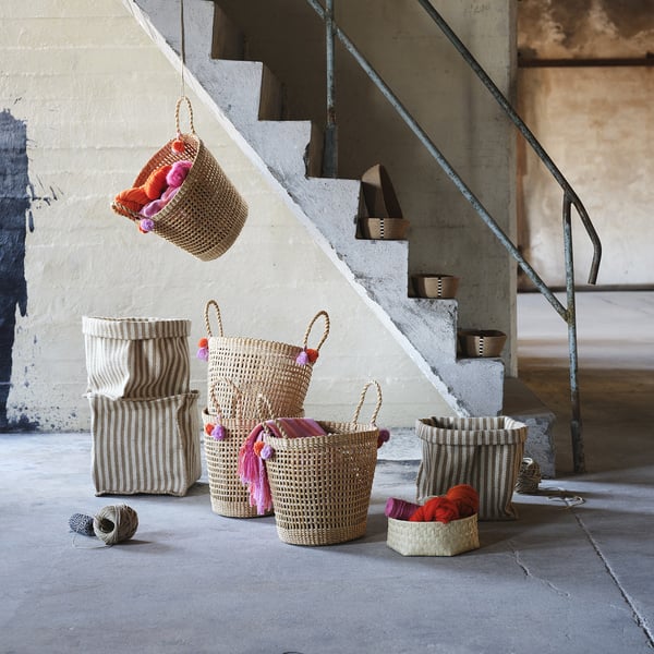 Several woven baskets in beige, dark beige, & stripes; some with tassels. They vary in size and shape, placed in front of steps.