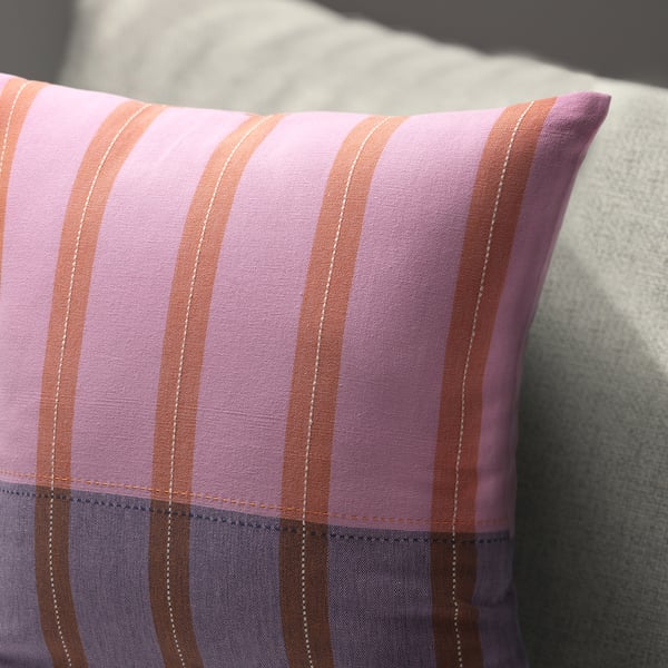Handwoven striped cushion cover with pink and orange hues on a light surface, soft texture and intricate stripes.