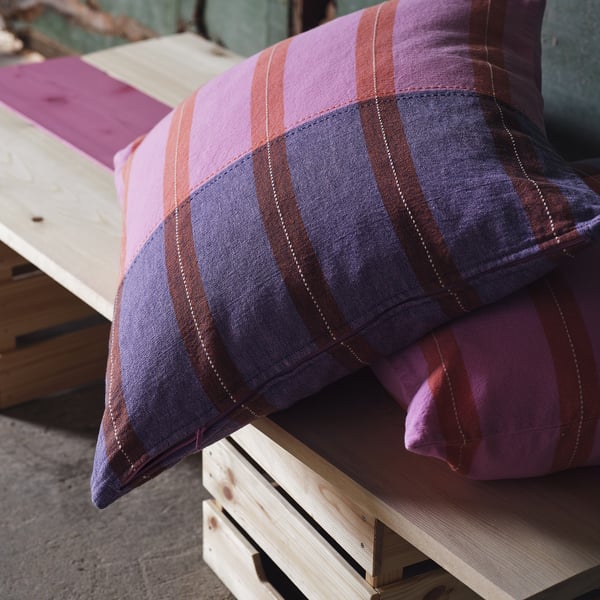 Pillows with striped pink and purple patterns are stacked on a wooden bench, showcasing their zip for easy removal.