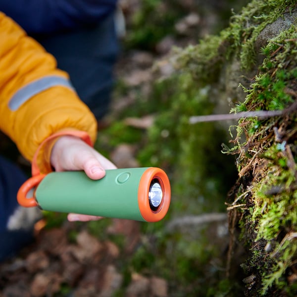 Child holding green and orange MAJBAGGE led torch, using string pull mechanism, outdoors.