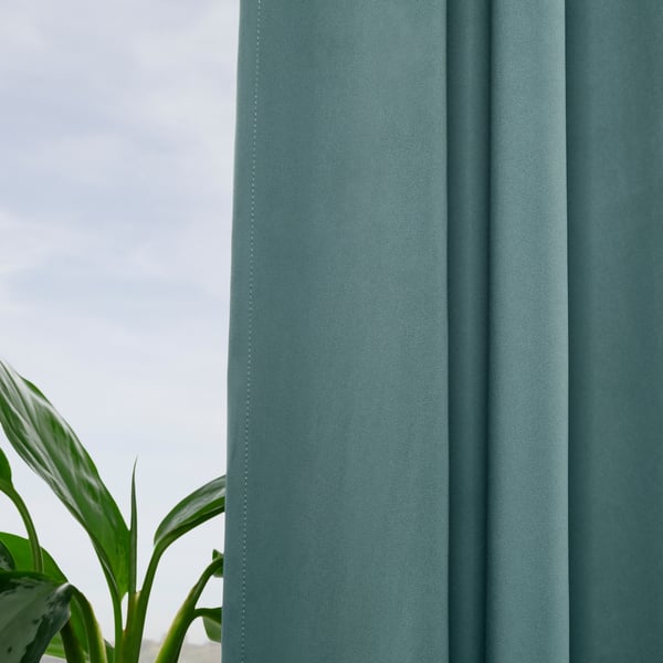 Teal MAJGULL curtains darken room, plant adds life.
