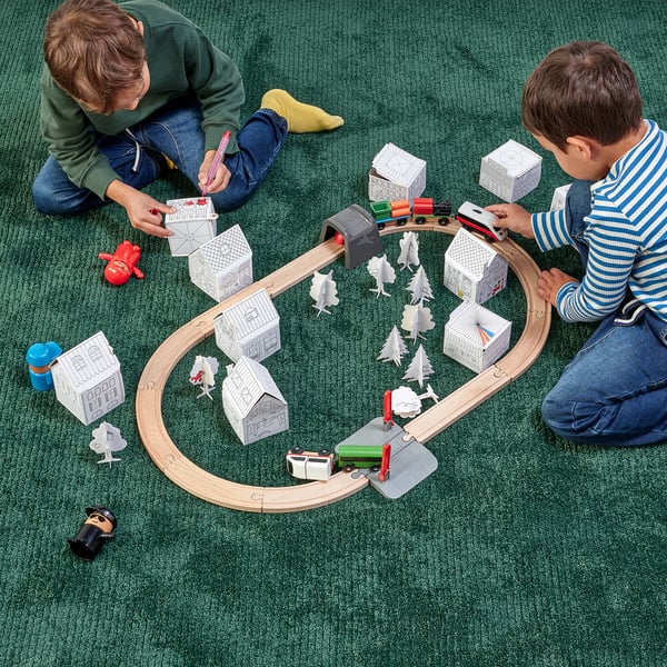 Two children playing with a MÅLA cardboard model town, train track, and vehicles.