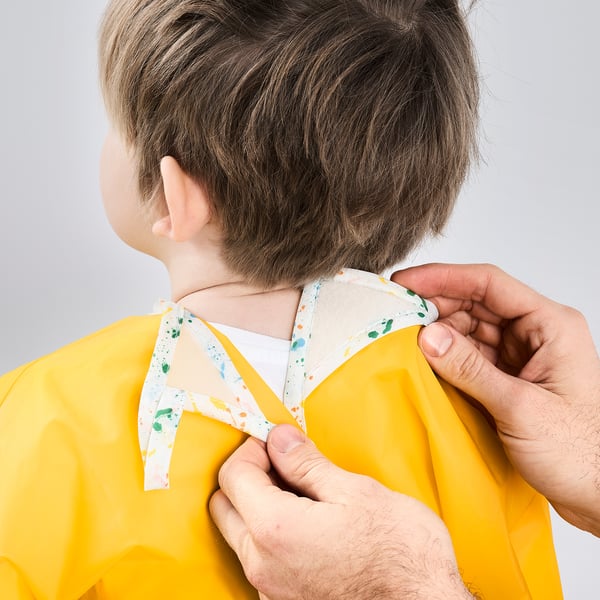 Child wearing yellow waterproof art apron, adult adjusting neck strap.