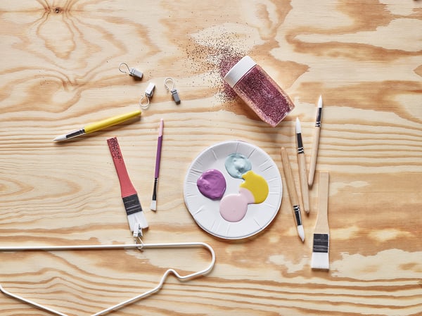 Art supplies: brushes, palette, paint, glitter on wooden table.