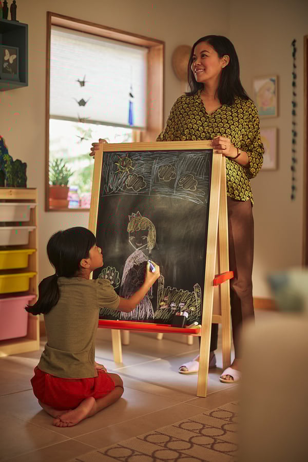 Child drawing with yellow MÅLA chalk on a blackboard.