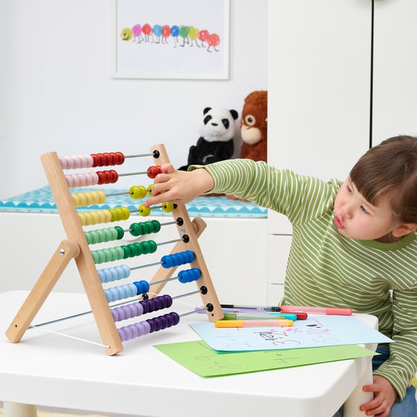 A child plays with a colourful abacus at a table, surrounded by drawing paper and pens.