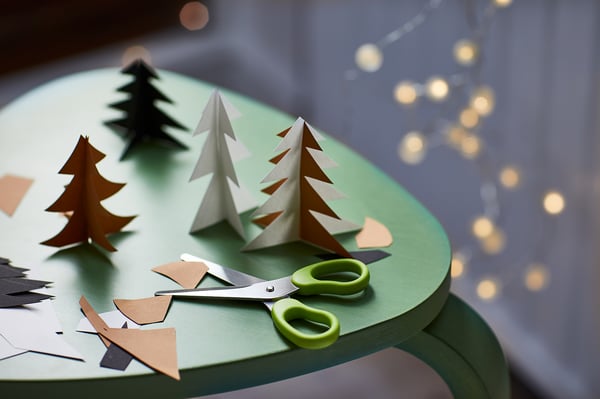 Craft scene with paper trees, green scissors on turquoise surface.