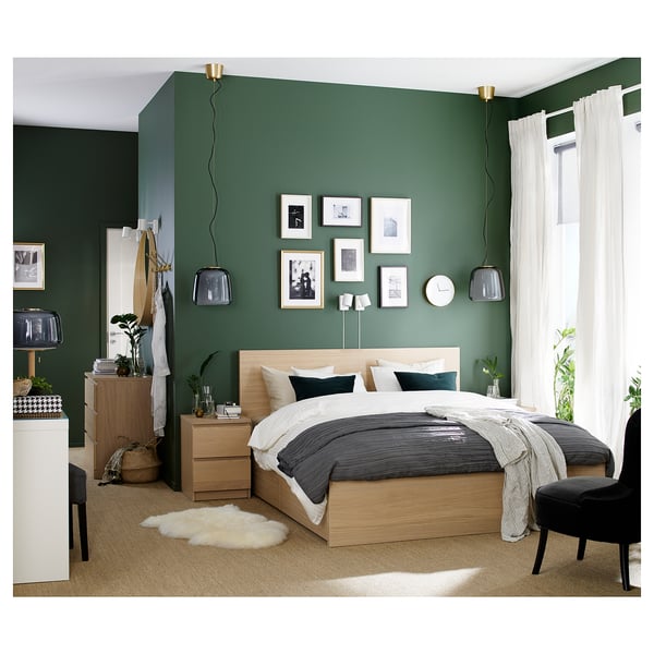 Cosy bedroom with green walls, white curtains, wooden furniture, and a large bed with a grey bedspread.
