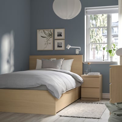 Modern bedroom with light wood MALM bed, grey bedding, blue walls, hanging white lamp, wall art, small bedside table, and window view.