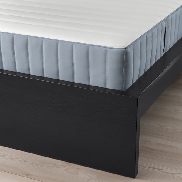 Close-up of grey mattress on black wooden bed frame with visible slats for air circulation.