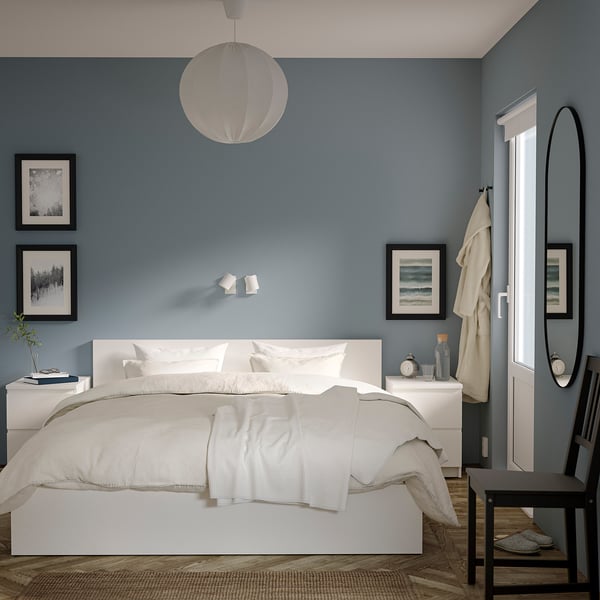 Minimalist bedroom with blue walls, white MALM bed, and nightstands; round lamp, mirror, and framed art.