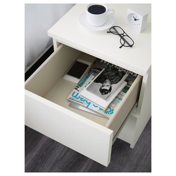 Open white bedside table drawer revealing magazines and a phone, suggesting storage function.