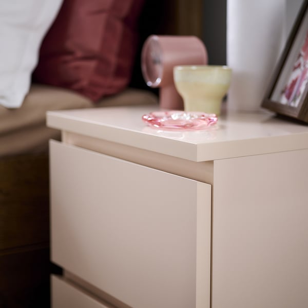Modern, light orange bedside cabinet with smooth finish. Top holds small colourful decor items.