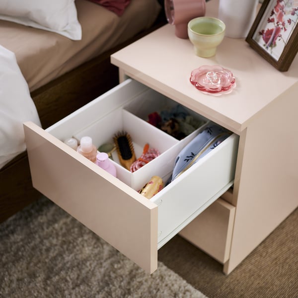 White bedside table drawer open, showing a hairbrush, bottles, and other items, with a light orange interior.