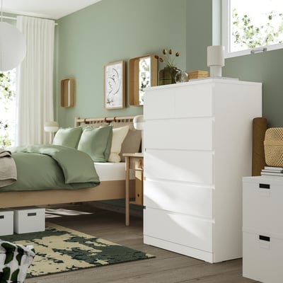 Modern bedroom with white MALM tall dresser, smooth surfaces, top drawers smaller, positioned near bed. Green walls, green bedding, wooden furniture.