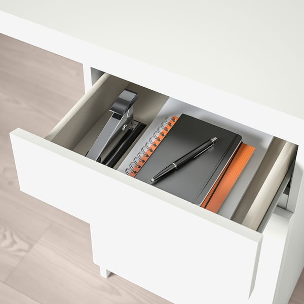 Open white desk drawer showing pen, notebook, and stapler, demonstrating organised storage.