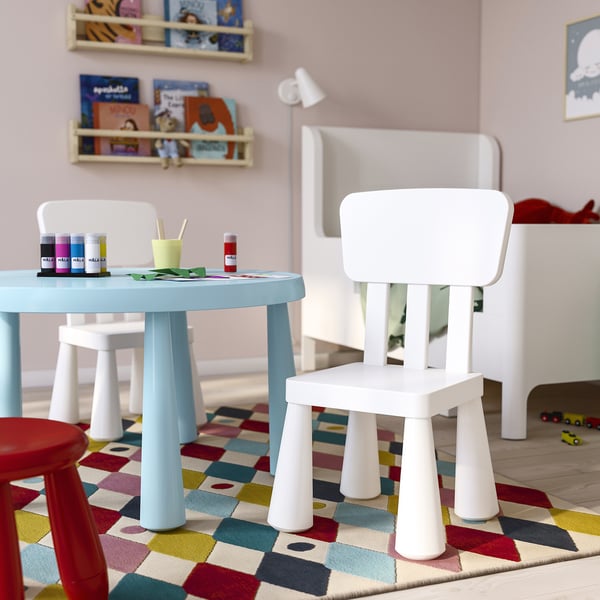 Childrens play area with white MAMMUT chair and table, colourful rug. Books and craft supplies on table, small car on floor.