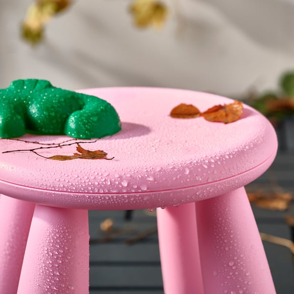 Bright pink stool with water droplets, green playdough, and dry leaves on top, perfect for childrens outdoor play.