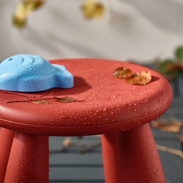 Red childrens stool with blue toy and leaves, outdoors