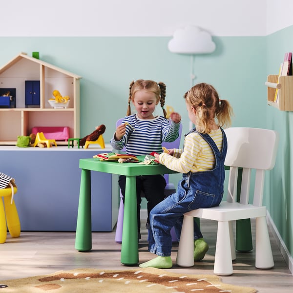 Two girls playing with toys at a green kids table.