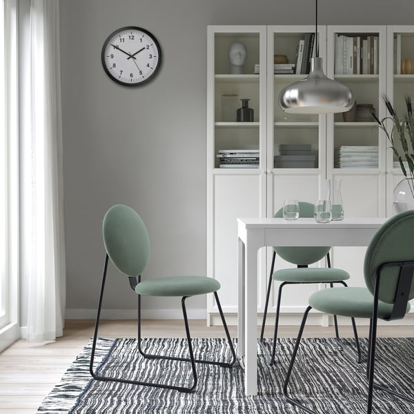 Modern dining setup with MÅNHULT chairs, clock, and bookcase, featuring green cushioned chairs and decorated bookcase.