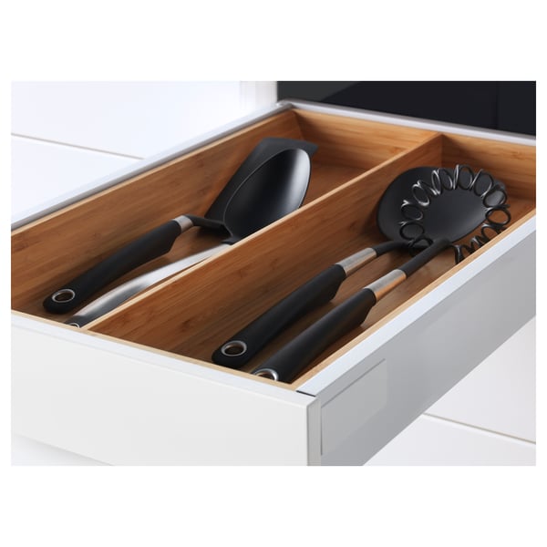 Wooden drawer in white cabinet holds black kitchen utensils: ladle, turner, and whisk, organised and ready for use.
