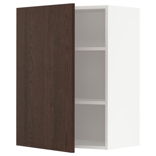 A white METOD kitchen wall cabinet with one dark brown door open, revealing two shelves inside. The door has solid wood edging and oak veneer finish.