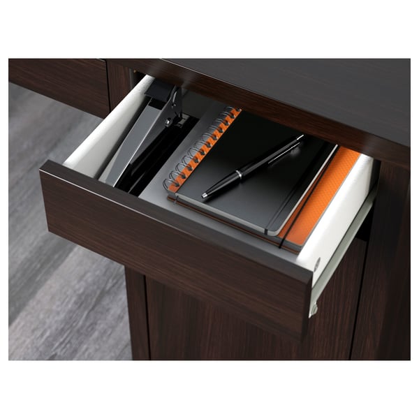 Open wooden desk drawer revealing a notebook and pen, fitted with cable management and adjustable shelves.