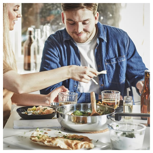 People cooking in kitchen with sauté pan.