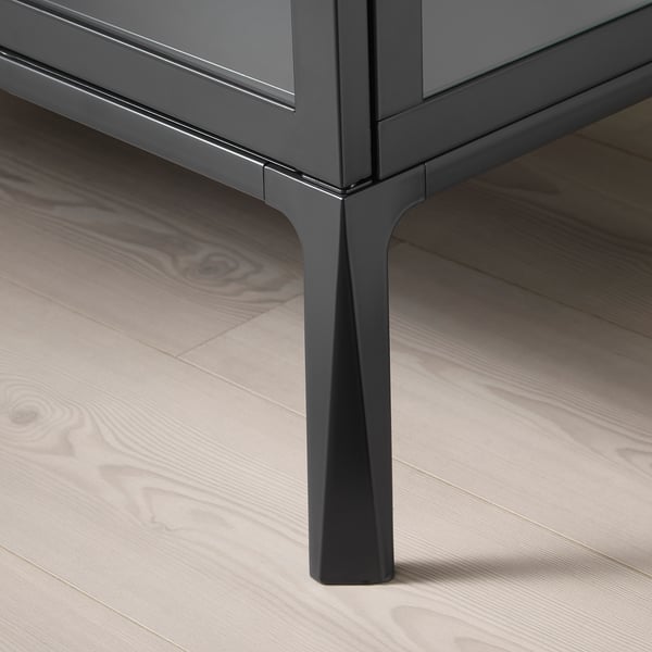 Black metal cabinet with angular leg on wood floor.
