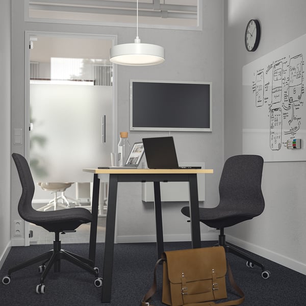 Small MITTZON conference table with black chairs, laptop, white light, and brown bag.