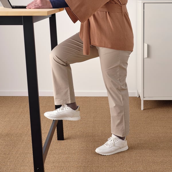 Person standing at high table using laptop, with one foot on a supporting footrest for comfort and stability.