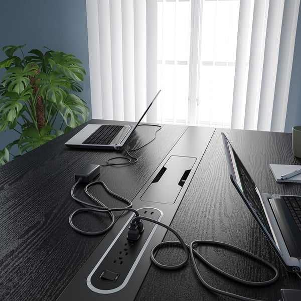 Black desk with built-in outlets, drei laptops, and plant; organised workspace.