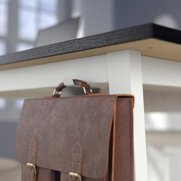 Brown leather bag hangs on high tables hook, with grey countertop and white leg visible.