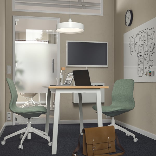 Modern office with MITTZON white table, green chairs, and wall-mounted tv. Bag and notes on table.