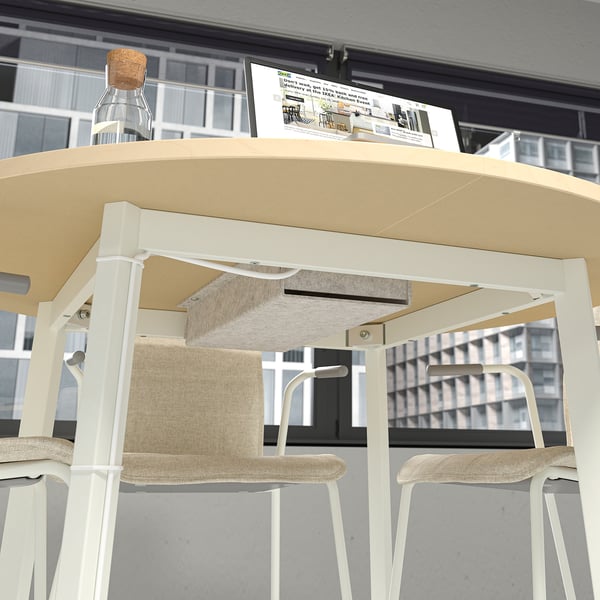 Underneath a round table on wheels, a felt cable tray holds cables, facilitating easy access for charging.
