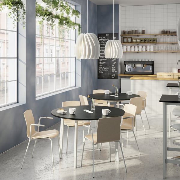 Modern café with round tables, light wood chairs, green plants, and coffee setup.