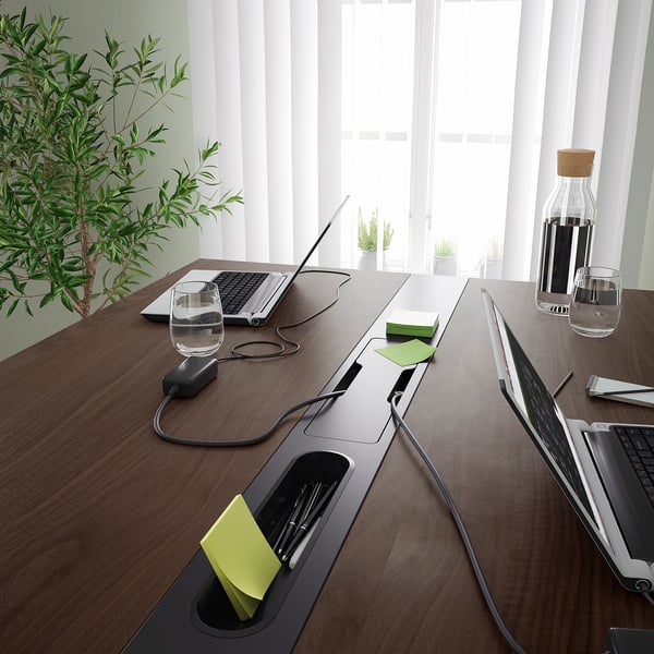 A conference table with built-in cable management and a laptop. The table includes a footrest for support and can be used for sitting or standing.