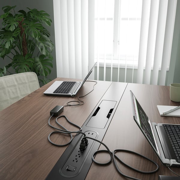 A modern conference table with laptops and plants. Built-in power outlet & cable management.