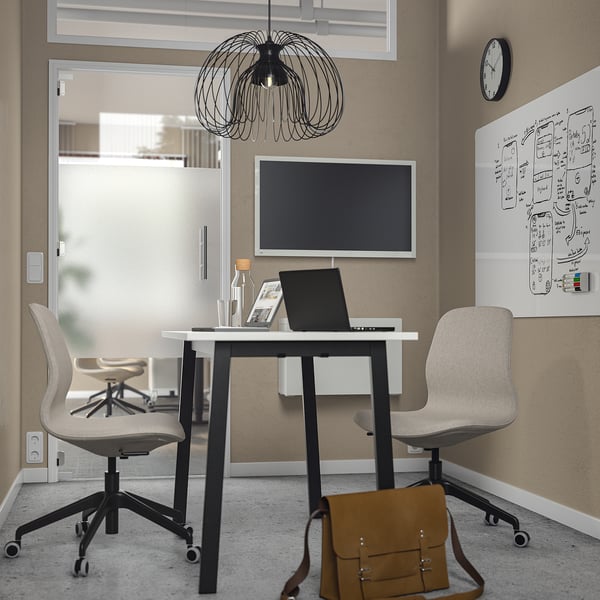 Modern office with MITTZON white desk, chairs, and monitor. A brown leather bag sits below. The room glass doors and a black pendant light.