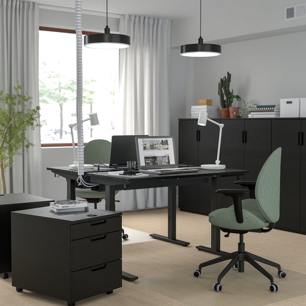 Home office setup featuring MITTZON black height-adjustable desk, green chairs, and black cabinets, with a large window and hanging lights.