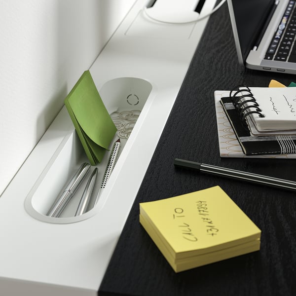 Organised office setup on a height-adjustable desk, showing notebooks, pens, and sticky notes.