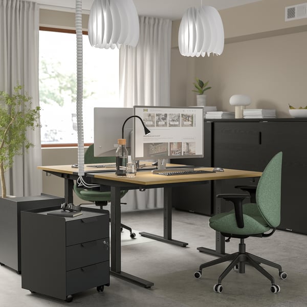 Adjustable desk, green chair, large screen, pendant lamps, black cabinet - minimalistic office setup.