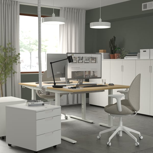 Modern home office setup with MITTZON white height-adjustable desk, computer, and ergonomic chair, surrounded by sleek cabinets and green walls.