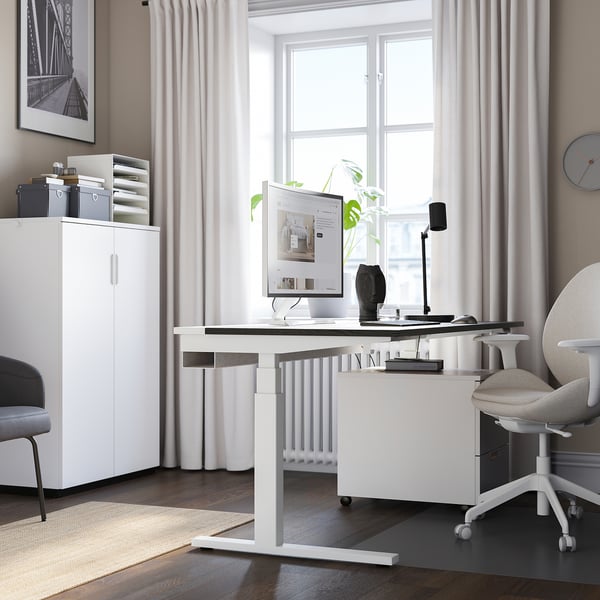 Modern home office with white MITTZON sit-stand desk, ergonomic chair, and storage unit.