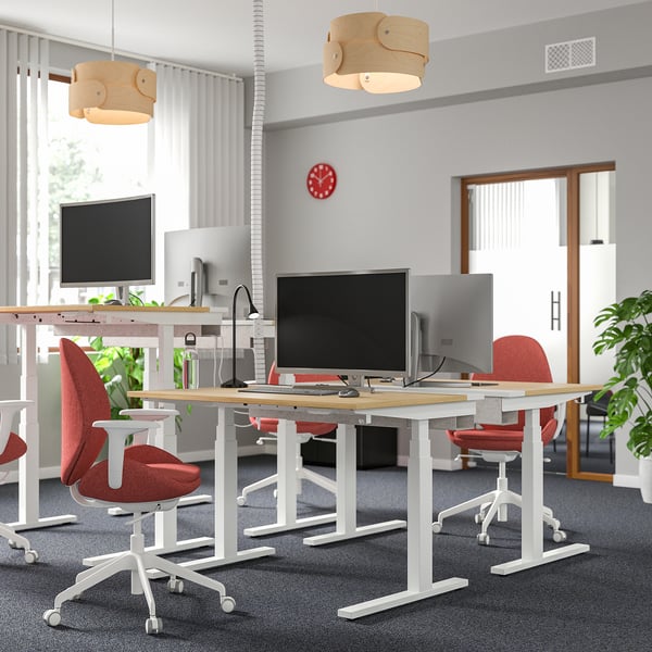 Modern office with MITTZON sit-stand desks, red chairs, wooden lamps, and a red clock.