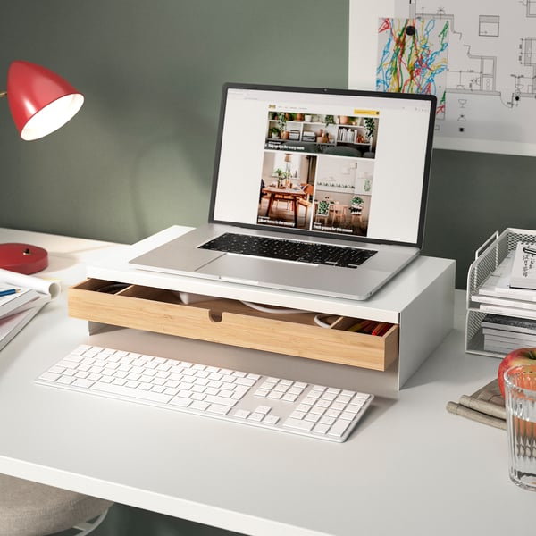 Modern workspace: laptop on stand, wireless keyboard, red lamp, apple, papers, organised desk.