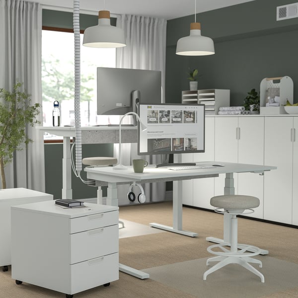 Modern home office featuring MITTZON white sit-stand desk with wide, adjustable underframe, dual monitors, chair, and storage cabinet.