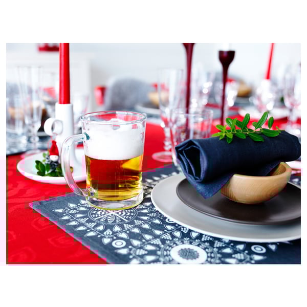 A red beer mug sits on a blue placemat, with a dark napkin and greenery.