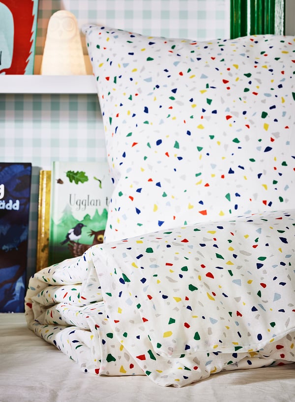 Brightly coloured terrazzo-patterned bedding on a cosy bed, featuring multicoloured squares on durable cotton.